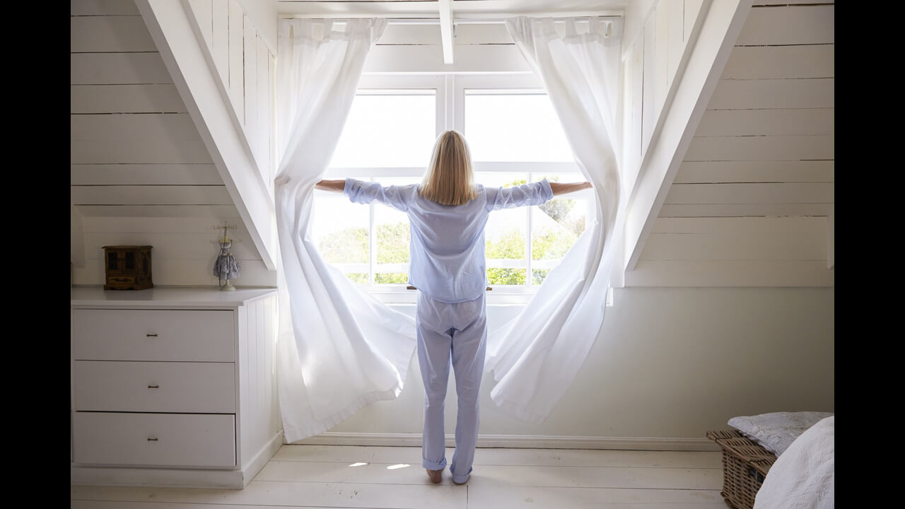 Rear-view of a woman opening curtains and looking out